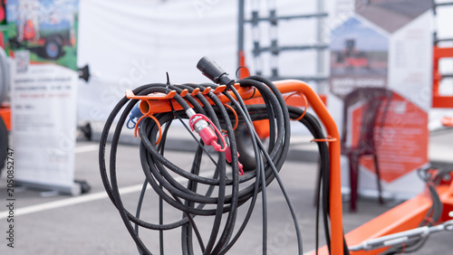 Canvastavla Coiled black cables and connectors hang on an orange metal stand in an indoor ex
