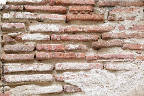 Close-up texture of an ancient weathered red brick wall with remaining white plaster and coarse mortar in the historic town of Elvas, Alentejo region, Portugal.