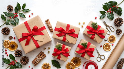 Multiple gift boxes wrapped in natural brown paper with vibrant red ribbon bows and blank gift tags arranged on a white wooden surface surrounded by festive holiday decorations and ornaments.