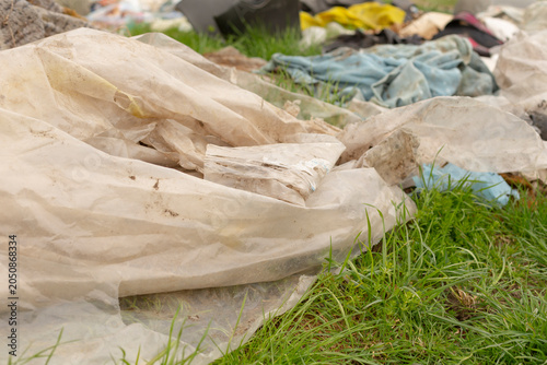 Quadro su tela Close-up view of discarded translucent plastic sheeting and crumpled fabric strewn across green grass