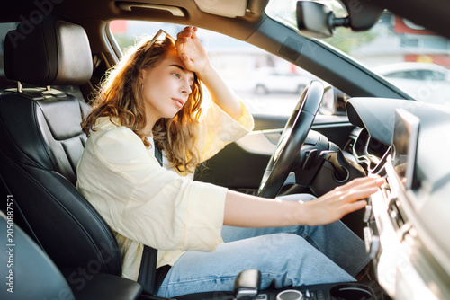 Obraz na plátne A young woman sits behind the wheel of a hot car