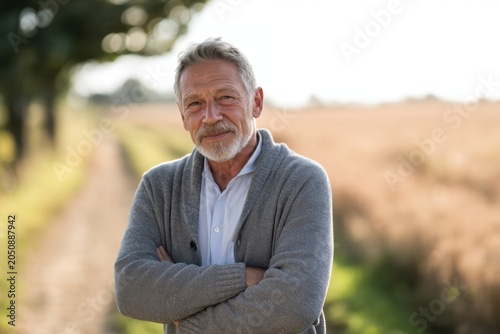 The mature man standing on a rural path with arms crossed and smiling