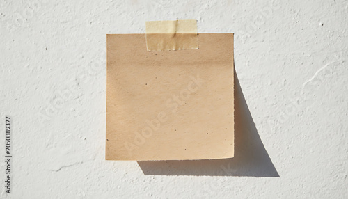 Brown paper note taped to textured white wall adhesive