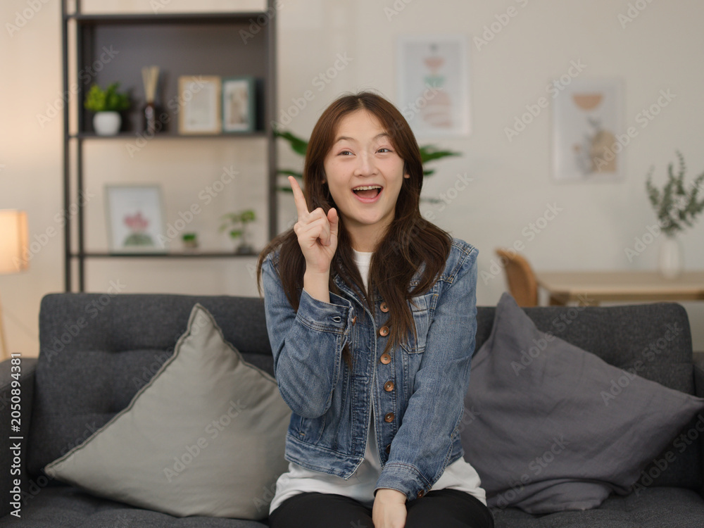 Obraz premium Excited Young Woman Raising Finger with Idea Gesture on Sofa