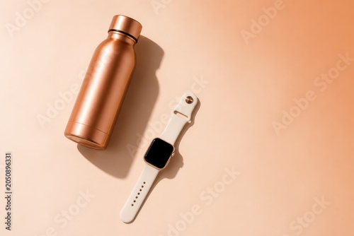 Copper water bottle and smartwatch on beige background minimalist product flat lay