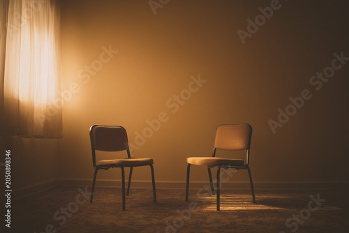 Two empty chairs facing each other in moody amber room with glowing curtain.
