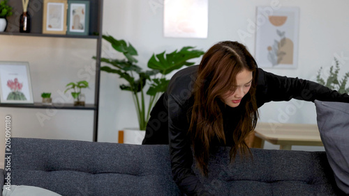 Quadro su tela Woman in Black Clothing Searching Behind Sofa Cushions in Living Room
