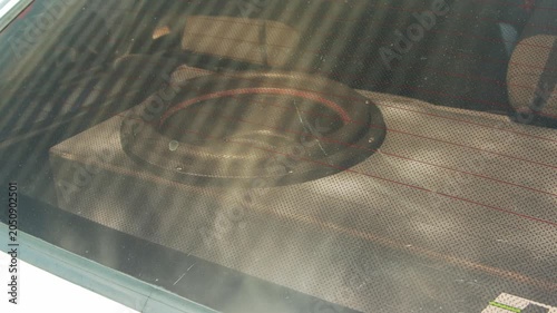View of powerful subwoofer speaker inside custom wooden box, installed in vehicle trunk, observed through rear window with defroster lines. Setup provides enhanced car audio bass.