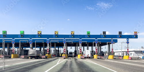 Highway toll plaza with traffic lanes, tollbooths, vehicles, transportation, travel and logistic infrastructure.