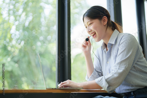 Foto Asian call center agent providing customer support, smiling and looking happy wh