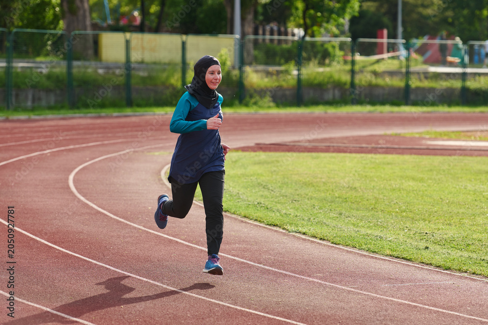 Fototapeta premium Young Muslim Woman Running on Outdoor Track in Hijab Training for Fitness and Healthy Lifestyle