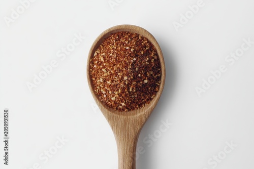 A wooden spoon filled with vibrant red chili spice on a light background.