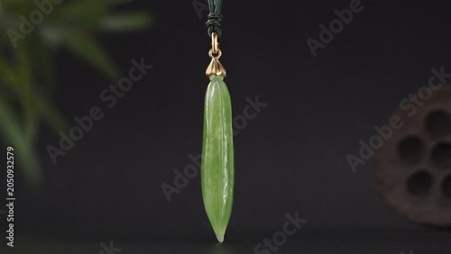 A slender green jade pendant shaped like a silique on a dark background.