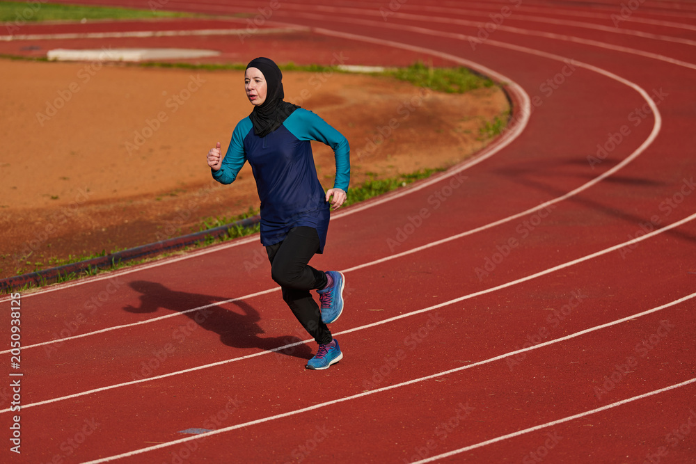 Obraz premium Muslim Woman Running on Outdoor Track in Hijab Wearing Athletic Clothes for Fitness Training