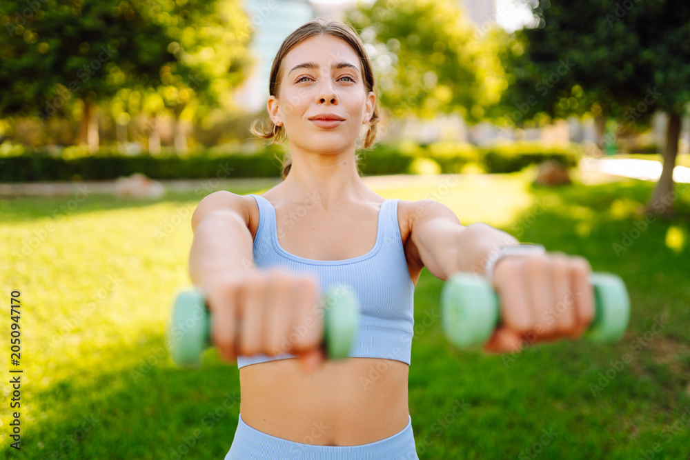 Fototapeta premium A smiling woman practices yoga on a pink mat in a sunny park. A young woman exercises or stretches at sunset. Concept of sports, relaxation, and meditation.