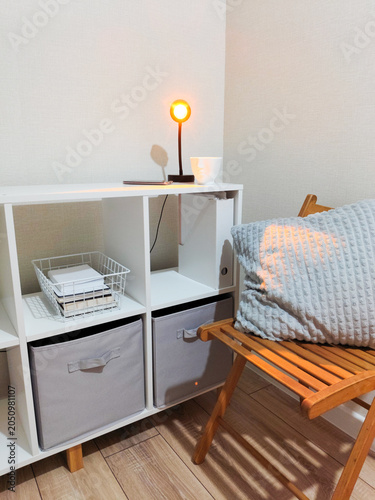 Student room interior with white bookshelf, comfy wooden chair and warm lamp glow. Cozy study space for generation z. Minimalist lifestyle design, academic environment and home workspace.