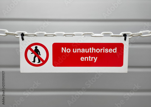 Cuadro en lienzo A red and white no unauthorised entry warning sign hanging from a white plastic chain, with a blurred grey industrial background