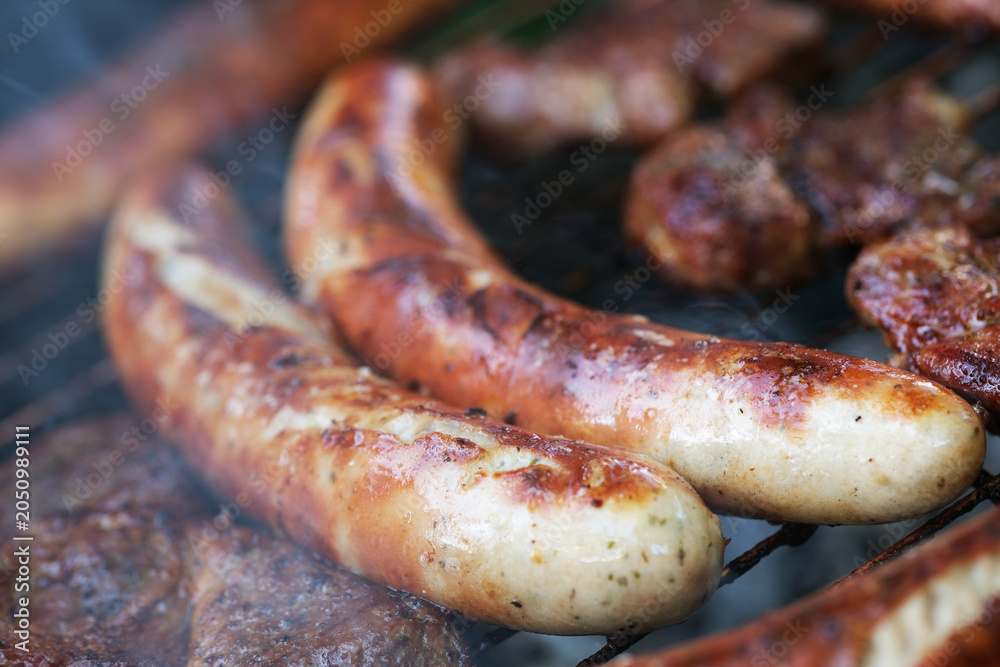 Fototapeta premium Zubereitung von Bratwurst und Schweinefleisch auf einem Holzkohlegrill.