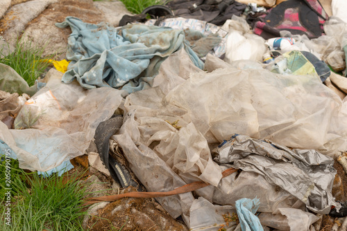 Bild auf Leinwand A close-up view of discarded clothing, torn plastic sheeting and scattered household rubbish piled on grass and rocky ground