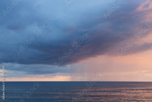 Dramatic Ocean Storm With Rain Shaft and Pastel Sunset Clouds Over Calm Horizon