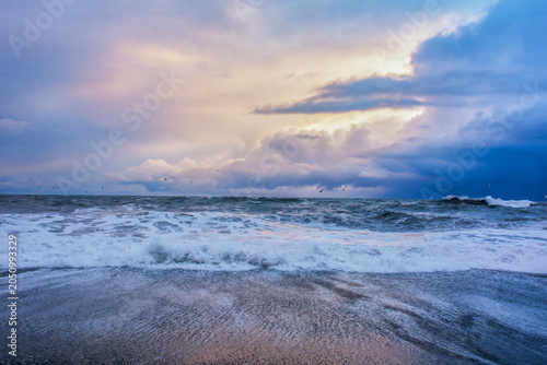 Powerful ocean waves crashing on a sandy beach under a dramatic sunset sky. High quality photo
