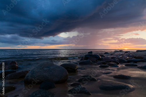 Stormy Sunset Over a Rocky Beach With Dramatic Clouds and Calm Sea Horizon