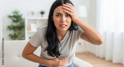 Young woman suffering from severe headache and stomach pain at home.