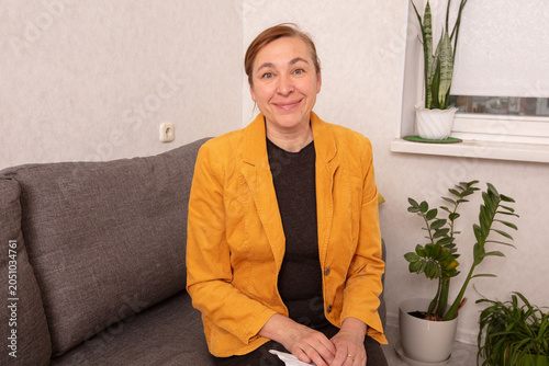Woman in yellow jacket sitting on sofa in light room with plants during daytime at home