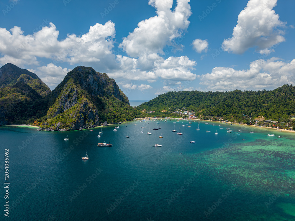 Obraz premium Aerial drone view of Corong Corong Bay in El Nido, Palawan, Philippines with turquoise sea, tropical mountains, anchored boats, and moving clouds above the coastline.