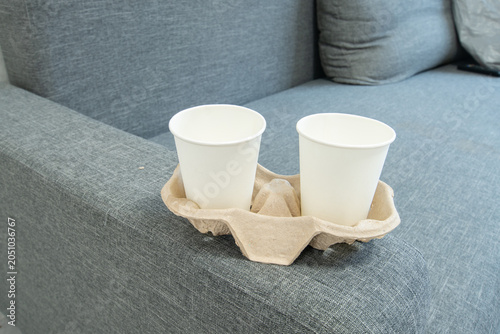 Cups placed on a gray sofa in a living room setting during daylight hours with a simple wooden tray
