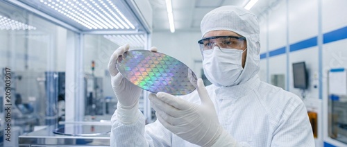 Technician in cleanroom suit examining semiconductor wafer in laboratory