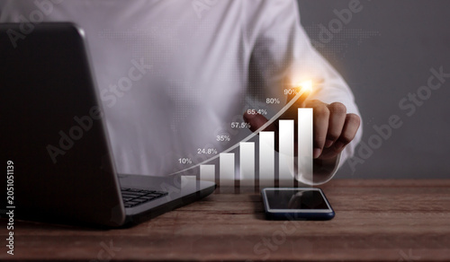 Young man with computer notebook and smartphone hand touching to visualize money growth The phone screen displays graphs and charts showing increasing investment and savings trends, increased account