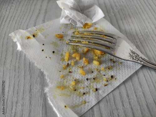 Used paper napkin with food crumbs and fork on wooden table, top view