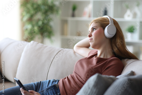 Serious young woman wearing headphone thinking listening audio
