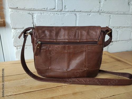 Back view of brown leather messenger bag with zipper pocket on wooden table