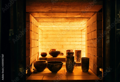 Photos Ceramic pottery bowls and vases placed inside a glowing industrial kiln with ora
