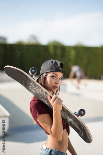Pretty skater woman with skate in sunny day looking at camera
