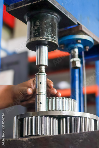 Fotografie An industrial technician hands aligning a metallic spindle pin under a hydraulic press piston rod to disassemble a heavy duty planetary gear assembly