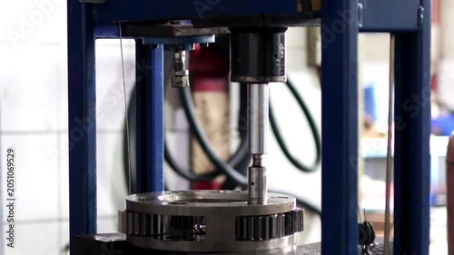 A close up vertical view of a hydraulic press piston rod pushing a metal spindle pin to disassemble a heavy duty planetary gear mechanism.