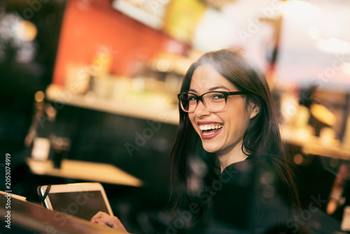 Pretty, brunette woman has a coffee in a bar while she looks at her tablet through the window