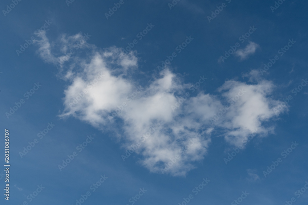 Obraz premium A single soft white cumulus cloud floating isolated on a vibrant clear blue sky background on a sunny day.