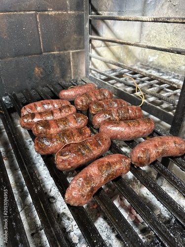 Traditional Argentine chorizo sausages grilling over an open barbecue in Patagonia, Argentina. A close-up food scene showcasing rustic outdoor cooking, smoky flavors, and regional cuisine.