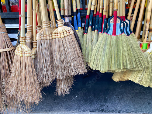 A variety of traditional brooms, including palm rib brooms and natural plant fiber brooms, displayed for sale in a household goods store. A concept of eco-friendly and organic household cleaning tools