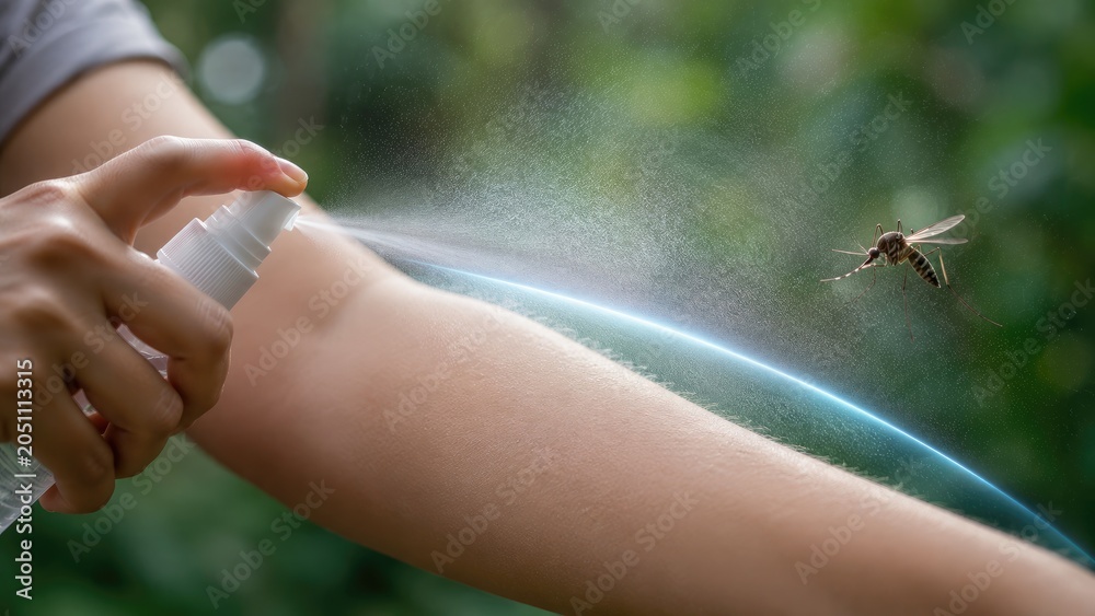 Obraz premium Hand spraying mosquito repellent mist on forearm as a mosquito approaches, outdoor close-up showing protection from bites