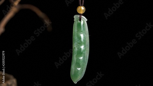 A slender green jade pendant shaped like a silique on a dark background.