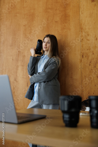 Smiling woman photographer with camera editing photos on laptop in office table