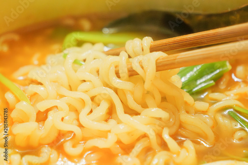 Close-up of Hot Ramen Noodles Lifted with Chopsticks in Golden Soup