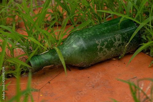 Fotografija Close up of a discarded green glass bottle on a red tiled ground overgrown with