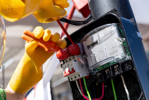 Foto Electrician in protective gloves and helmet installing or repairing an electricity meter board close-up