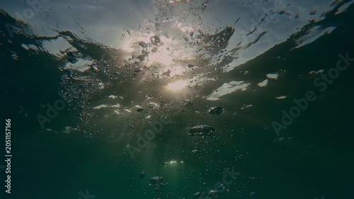 Sea waves and bright sunshine on water, trickle of air bubbles slowly rising to the surface in morning light (golden hour) backlighting by vivid sunbeams, natural marine background